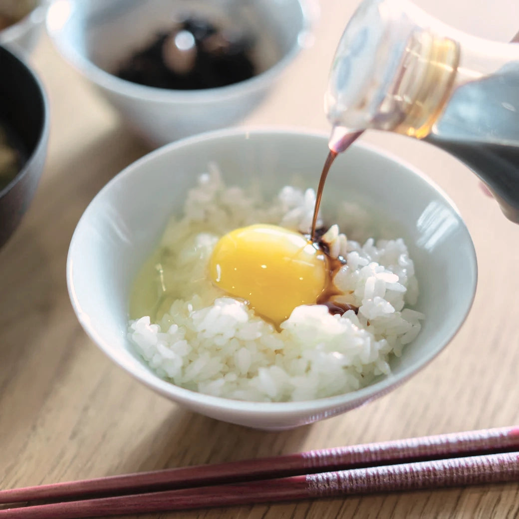 炊きたてのご飯にのせた黄身に醤油をかけているところ