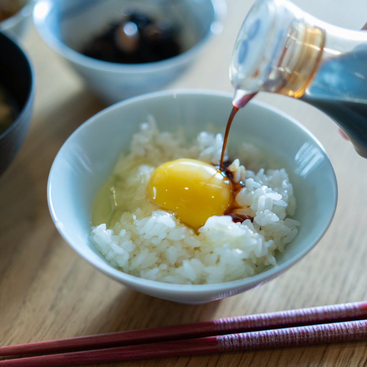 炊きたてのご飯に平飼いたまごをのせ、醤油を注いでいるところ