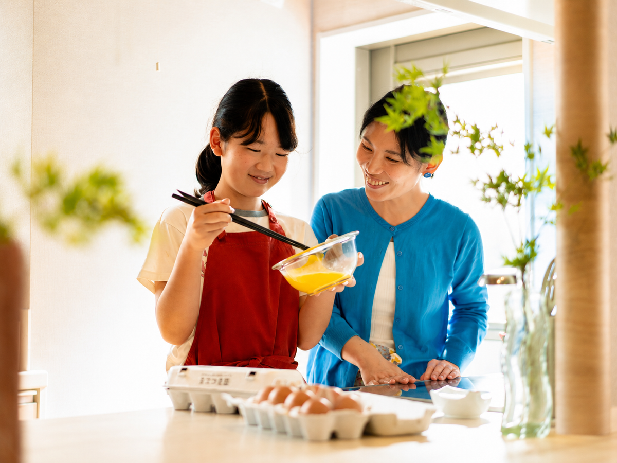 台所で娘が卵を混ぜ、母親が見守る様子